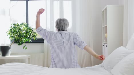 Senior-Woman-Stretching-on-Bed-at-Home-Bedroom.old-age-and-people-concept--senior-woman-in-pajamas-sitting-and-stretching-on-bed-at-home-bedroom