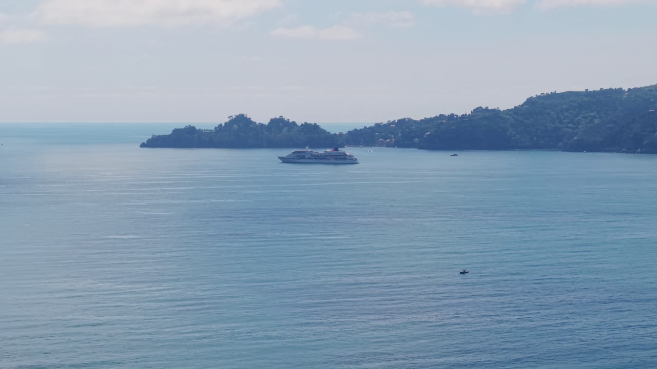 Aerial shot of Mediterranean Sea with a cruise ship, calm water, and distant island in Italy