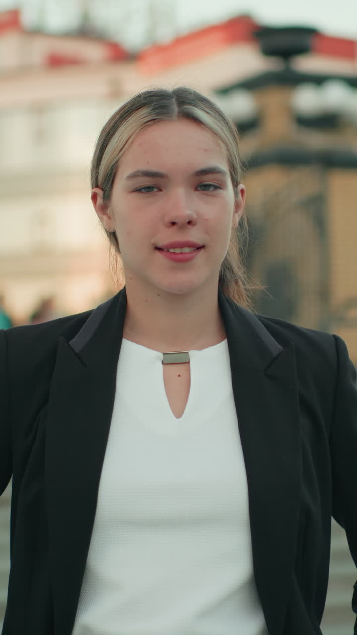 Elegant lady poses with hands in pockets, exuding confidence and calm in modern urban environment with architectural features and steps behind her