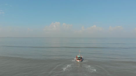 falling follow drone shot of small colourful indian fishing boat going out to sea