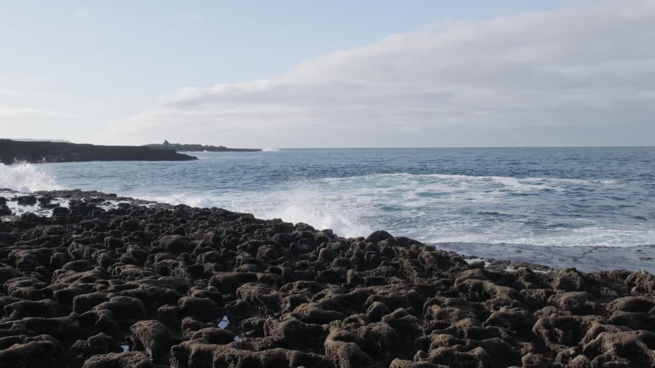 Rugged, rocky coastline breaks waves with large splashes. Ocean waves rolling in from afar and breaking on cliffy shore. Slow motion footage on coast of Ireland.
