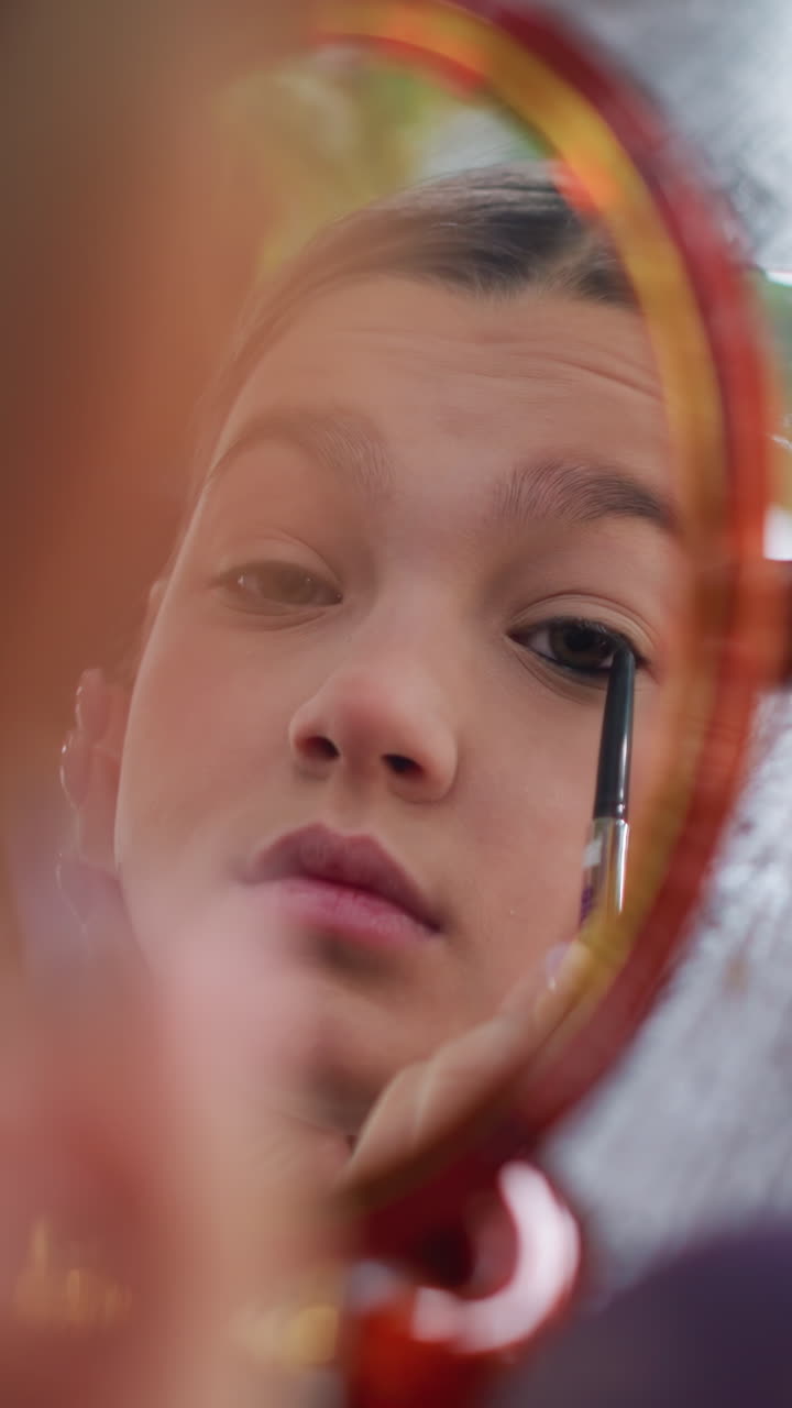 Contemplative moment captured with outdoor lighting, Natural glow enhances thoughtful expression of young girl, Young woman uses antique mirror to carefully apply eyeliner outdoors
