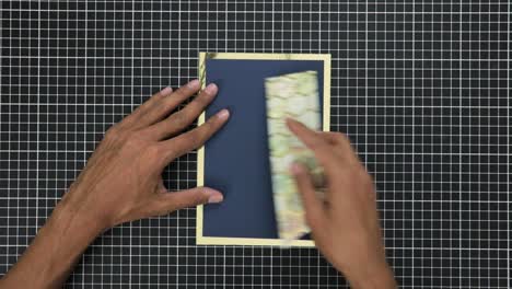 hands crafting a gift card with gold foil on a gridded cutting mat, overhead view