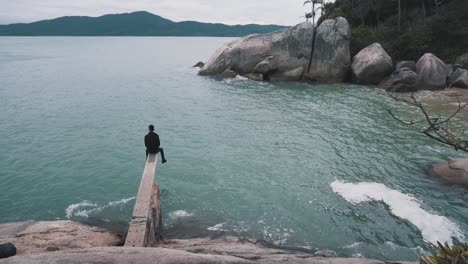 young man sitting relaxing on a trampoline above the water of a secret brazilian beach on cloudy day