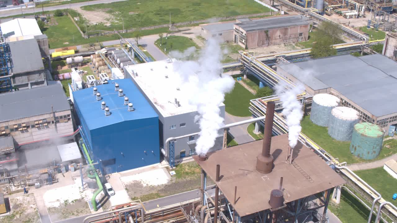 A top-down aerial shot orbits directly above an industrial smokestack as it releases plumes of white smoke and steam, showcasing factory emissions and air pollution