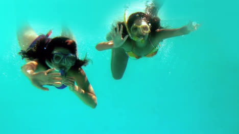 amigos felices saludando a la cámara bajo el agua usando snorkels