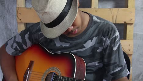 asian male teen wearing fedora tuning a classical guitar