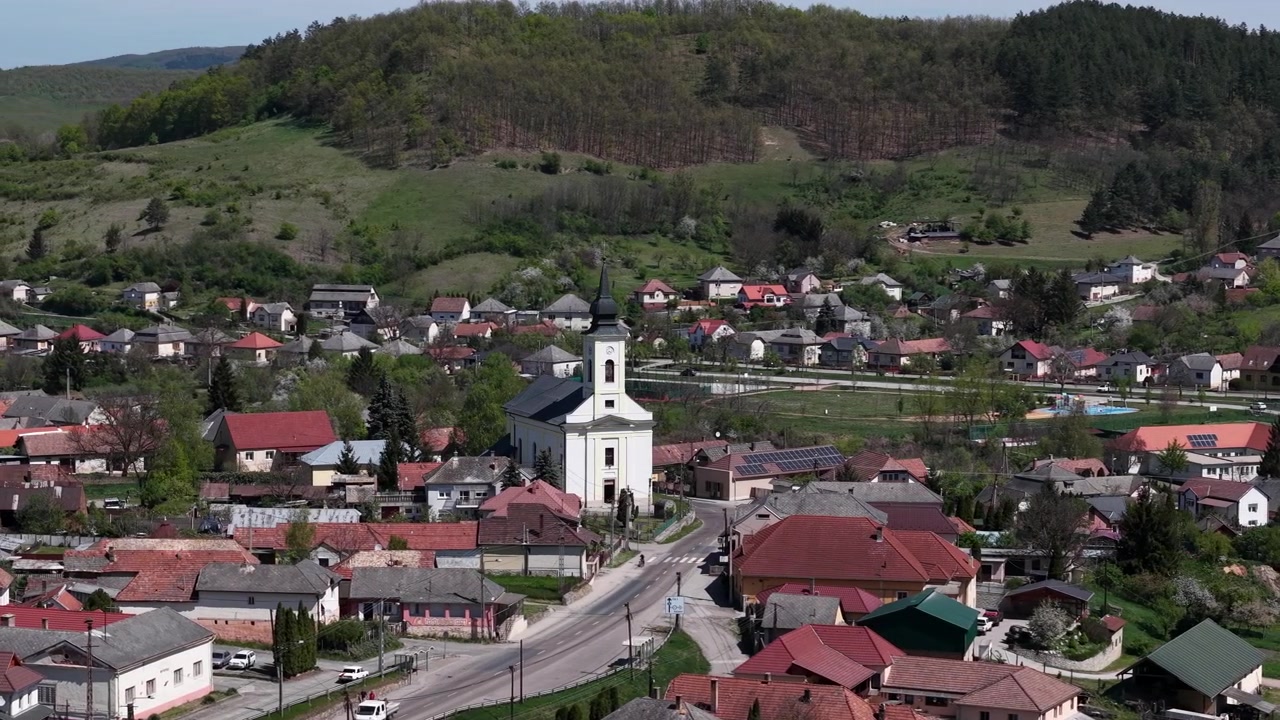 Pohled z výšky odhaluje malebnou venkovskou vesnici s výrazným kostelem, uhnízděnou uprostřed živých zelených kopců během krásného jarního období.