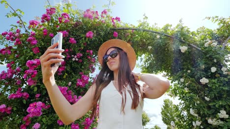 stylish lady poses with phone under blooming archway in european palace garden