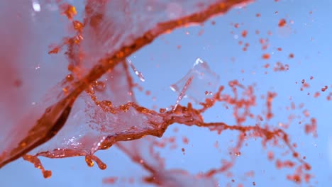las imágenes en cámara lenta capturan una copa de vino rompiéndose contra un telón de fondo azul, retratando el efecto del vidrio roto con toque artístico