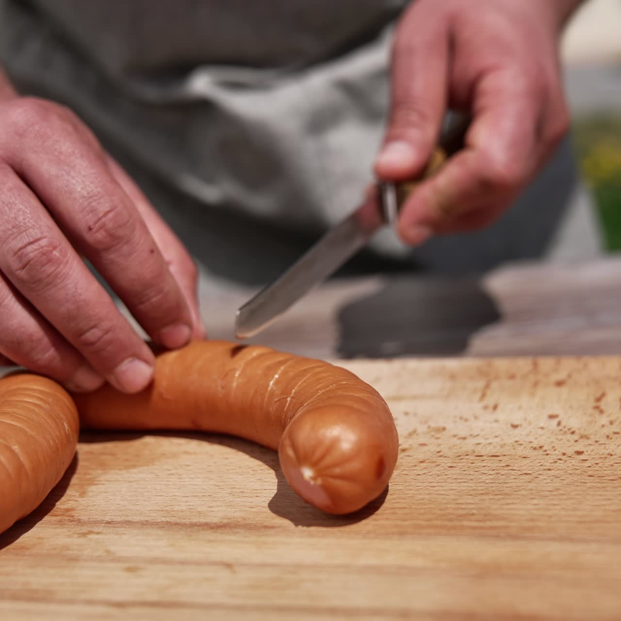 Mannenhanden snijden worst om op vuur te koken. Sappige worsten bereiden voor de barbecue in de buitenlucht. Koken in de natuur. Close-up.