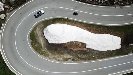 drone shot in a curve of the furkapass, valais, with a car and a motorbike in switzerland.