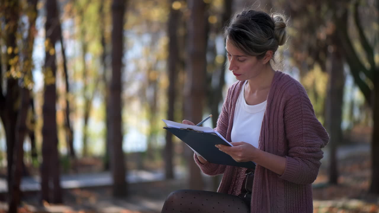 Woman writing on paper on a bench in the park on a sunny day