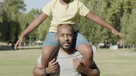 father carrying his son on shoulders while walking in park.