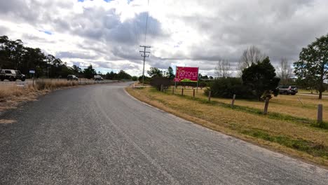 a vehicle travels a winding country road in stanthorpe, queensland, passing a roadside orchard sign under cloudy daylight. smooth camera movement, natural rural setting