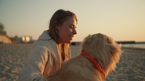 Close-up-shot-of-a-girl-and-her-light-colored-dog-sitting-on-a-sunny-beach-in-the-morning