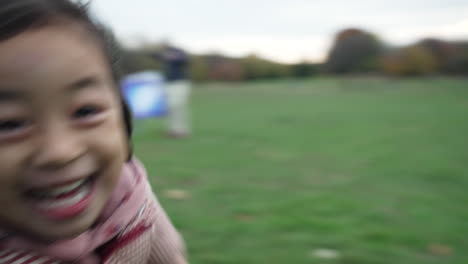 Close-up-view-of-a-girl-and-her-friend-smiling-and-running-after-the-camera-in-the-park-on-a-wintry-afternoon