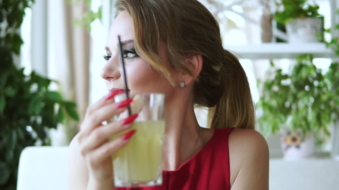 mujer joven con el pelo largo rubio sentada en la mesa y relajándose en el café y bebiendo sabrosa limonada. disparo en cámara lenta