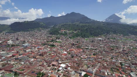 Drone-aerial-footage-of-urban-central-american-colonial-city-Quetzaltenango-Xela,-Guatemala-with-colorful-rooftops-and-cityscape-surrounded-by-mountains-and-volcano