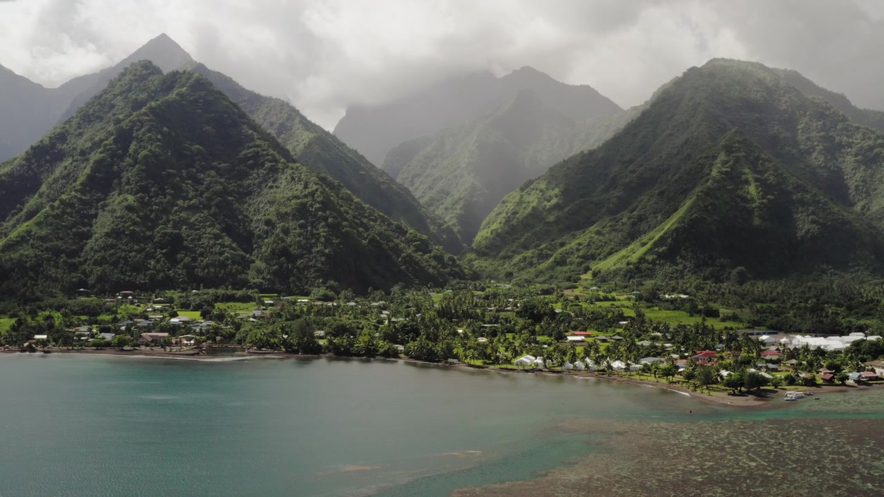 Teahupoo, Tahiti yakınlarındaki sisli zirveler ve taro tarlaları üzerinde süzülen hava dronu, vadi tabanını kıyıya doğru takip eden teraslı yeşil tarlalar