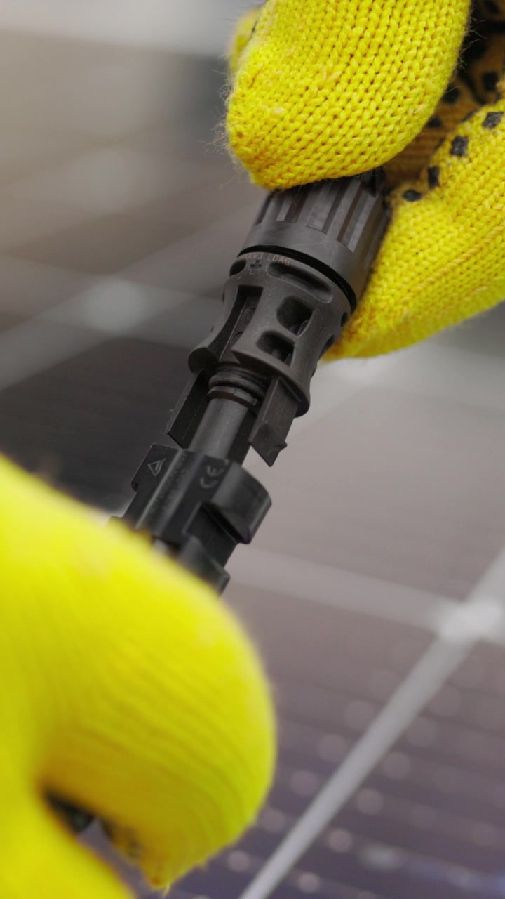 Close-up de uma pessoa usando luvas amarelas conectando um conector de painel solar, vídeo vertical