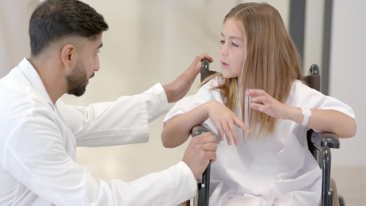 Médico y paciente feliz en silla de ruedas hablando en la sala del hospital, a cámara lenta