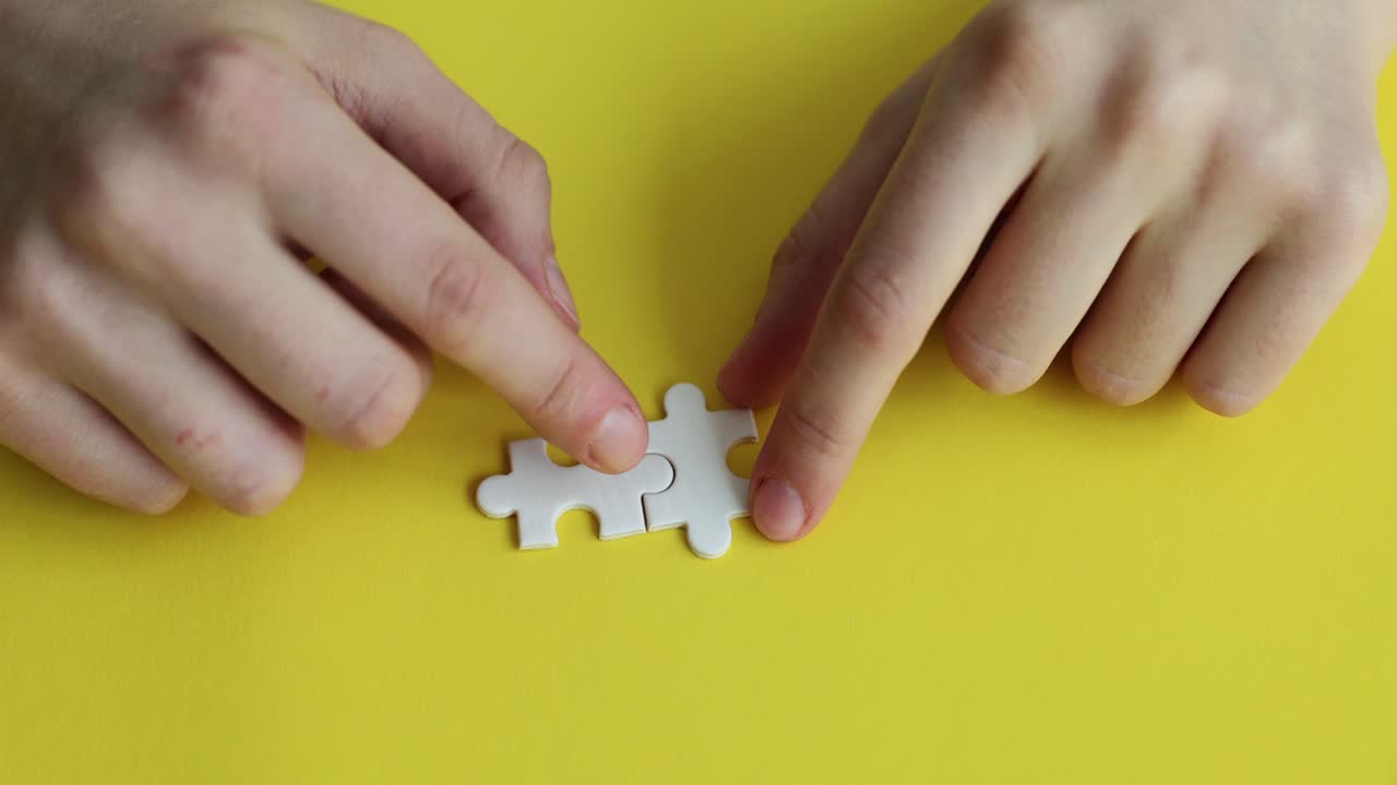 Hands connecting two white puzzle pieces on a yellow background