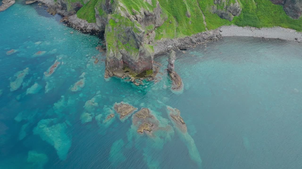 Aerial tilts up peninsular landscape in Shakotan, Japanese sea along green cliffs, natural environment