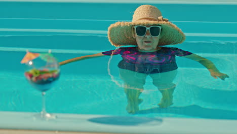 senior woman relaxing in pool with cocktail