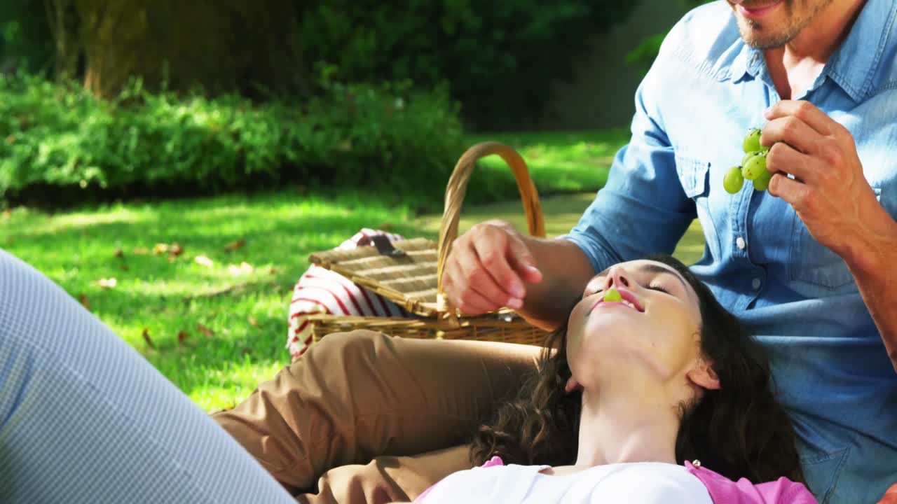 한 남자 가 공원 에 있는 여자 에게 포도 를 먹이고 있다