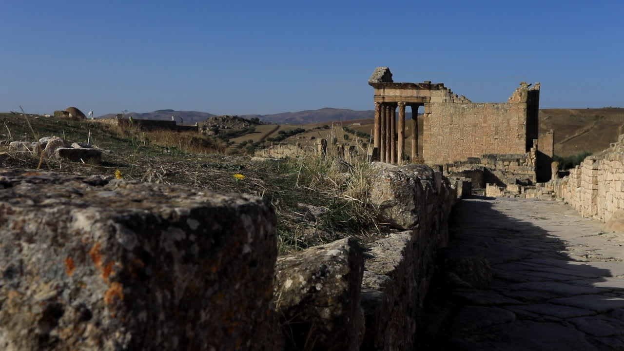 antiguas ruinas romanas en dougga con detalladas texturas de piedra y líquenes, bajo un cielo azul claro