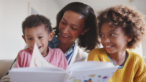 African-American-mum-sitting-on-sofa-reading-to-her-two-kids,-low-angle,-close-up