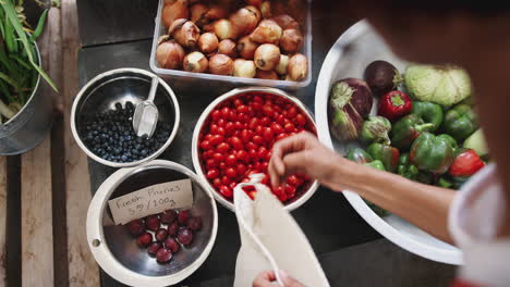 primer plano de una mujer poniendo tomates en una bolsa de algodón reutilizable en una tienda de comestibles sin plástico