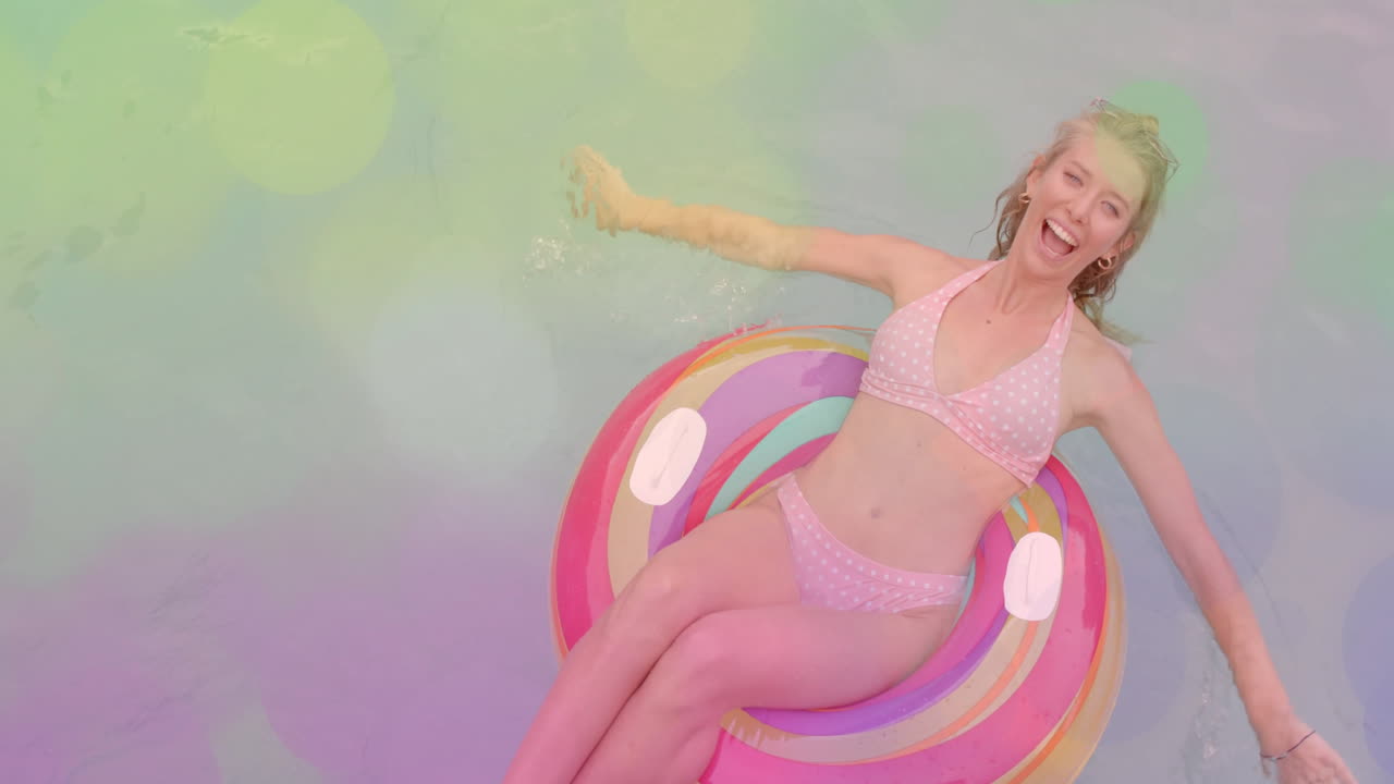 Smiling woman relaxing on colorful float in pool over bokeh lights animation