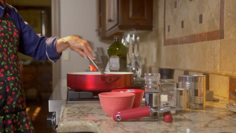 Movimiento-Deslizante-De-Una-Mujer-Que-Revuelve-La-Comida-Para-Cocinar-En-Una-Sartén-Roja-En-La-Estufa