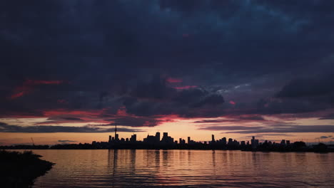 tilt down from an ominous sky tinged with pink clouds to a stunning lake ontario and toronto skyline silhouetted at twilight