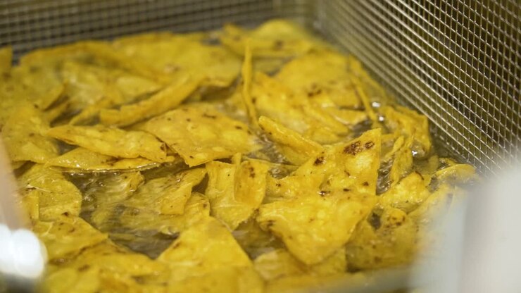 Tortilla chips in frying oil, sizzling nacho crisps in hot oil, slow motion