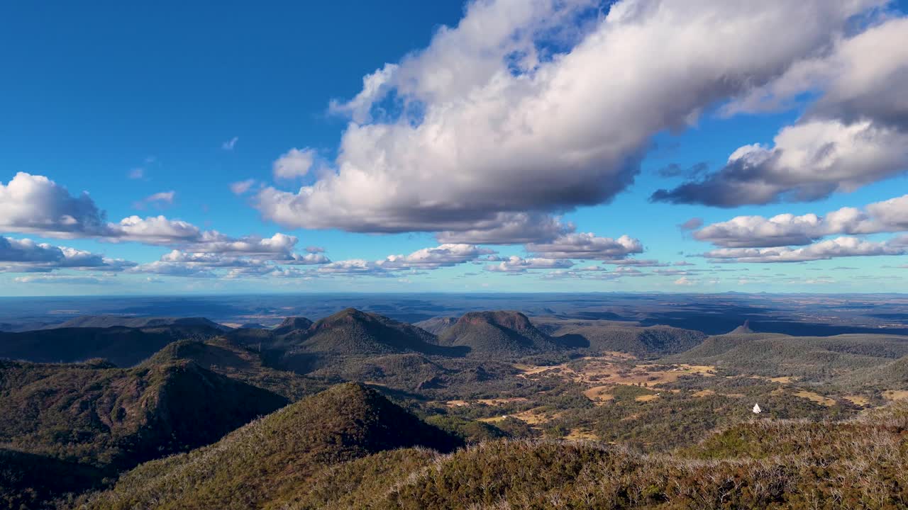 Drone captures sweeping aerial views of Warrumbungle National Park’s rugged mountain landscape, gum forests, and dramatic clouds in golden late afternoon sunlight