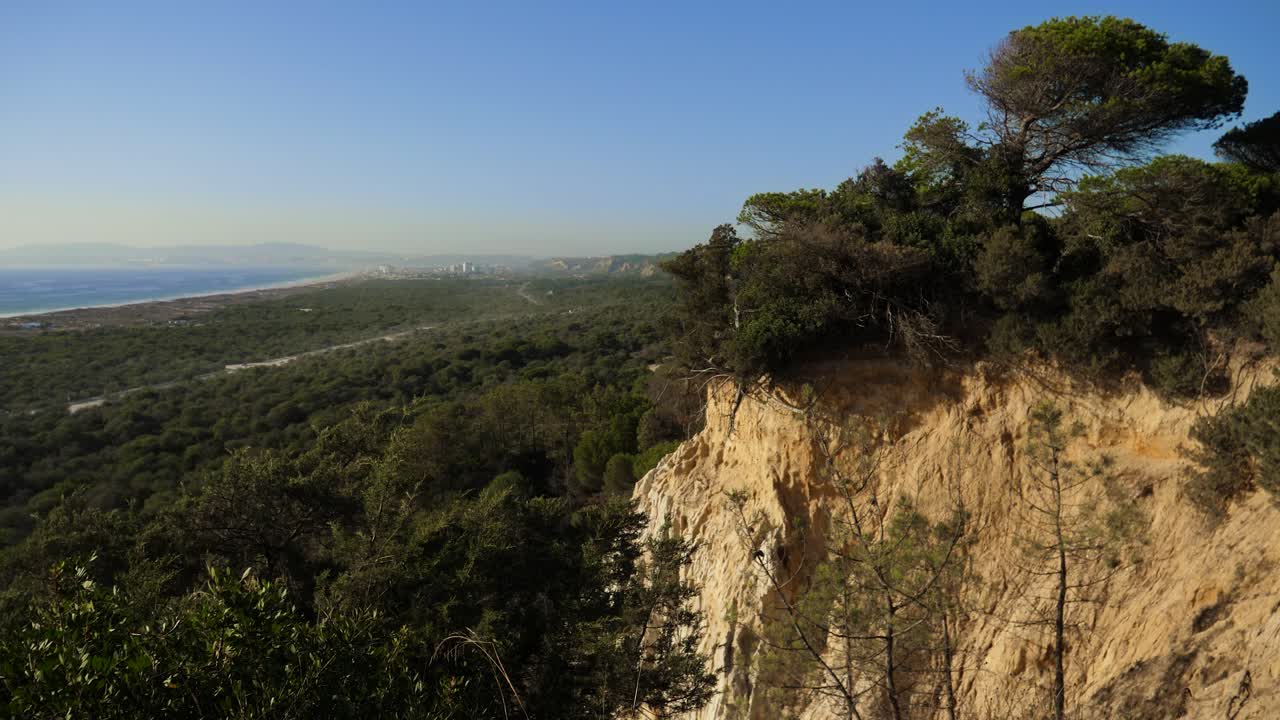 paisaje de acantilados costeros, vegetación de matorrales, océano y ciudad en la distancia