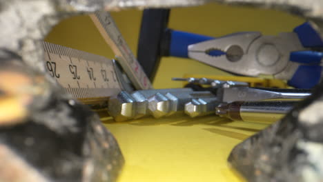 primer plano de dolly que muestra herramientas para el trabajo, medición de material, destornillador y martillo en la superficie amarilla