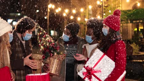 happy multiethnic friends talking and holding presents on the street while it¬¥s snowing in christmas