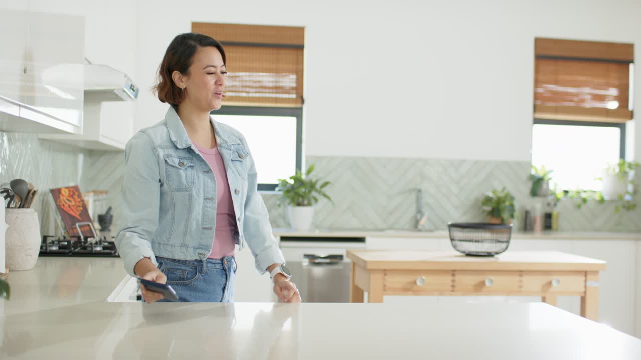 Donne diverse intorno all'isola cucina, una tiene in mano il telefono, l'altra entra portando la spesa, suscitando sorrisi