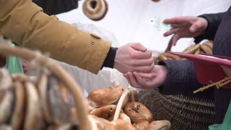 costumer buying ring shaped bread rolls seasoned with poppy seeds in a city fare. hand paying money for bagels, bread ring