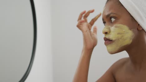 Happy-african-american-woman-apply-beauty-mask-on-face-in-bathroom