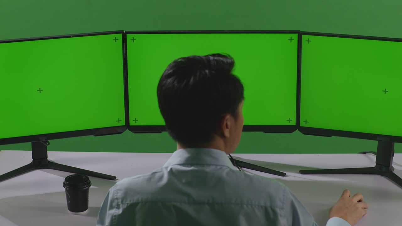 그린 스크린 스튜디오에서 여러 컴퓨터 모니터를 모의로 작업하는 아시아 남자의 뒷면
