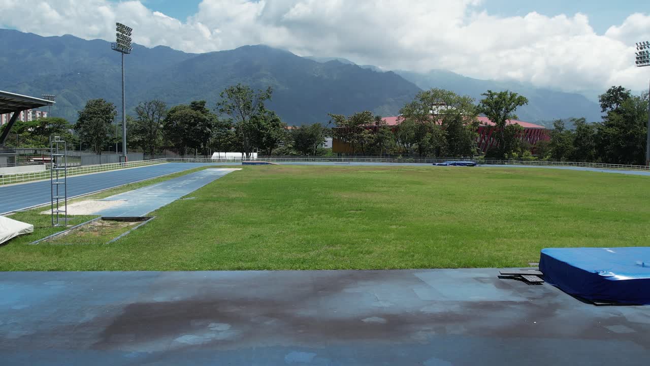 Drone footage showing lateral movement over an athletics track with the Coliseum in the background. The drone gradually gains altitude before moving forward towards the Coliseum.