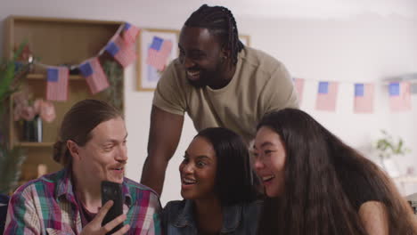 amigos en casa celebrando con la fiesta por el día de la independencia de estados unidos el 4 de julio mirando fotos en el teléfono móvil