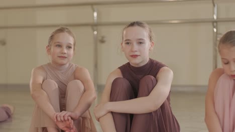 a group of young ballet students in black dancewear practicing positions in a spacious ballet studio with wooden flooring and wall-mounted barres. focused expressions and synchronized movements.