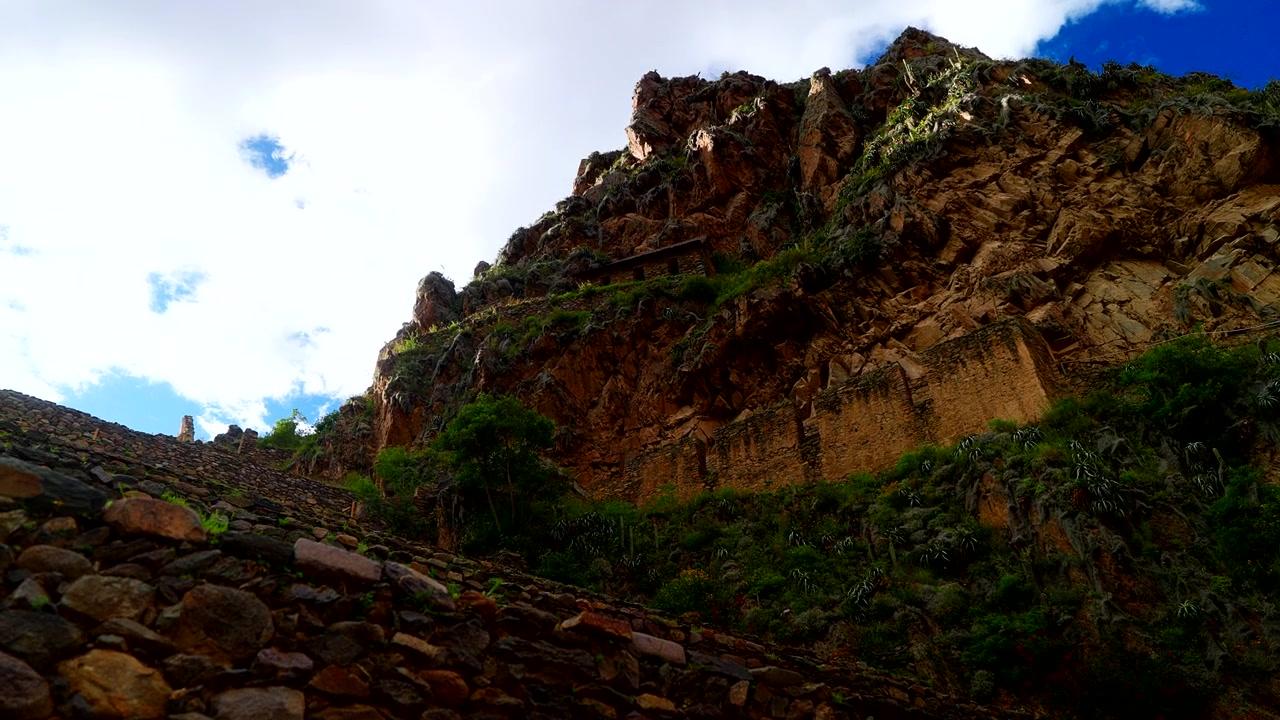 Ruinas incas de Ollantaytambo bajo acantilados escarpados en el Valle Sagrado de Perú, bajo un cielo azul, toma de establecimiento ascendente