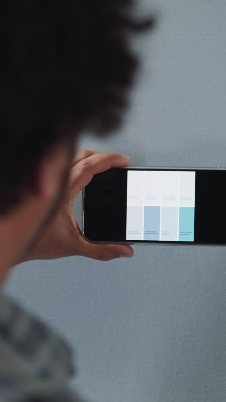 African-American designer chooses color shade for flat wall painting on smartphone screen close back view. Black decorator with mobile phone works in premise